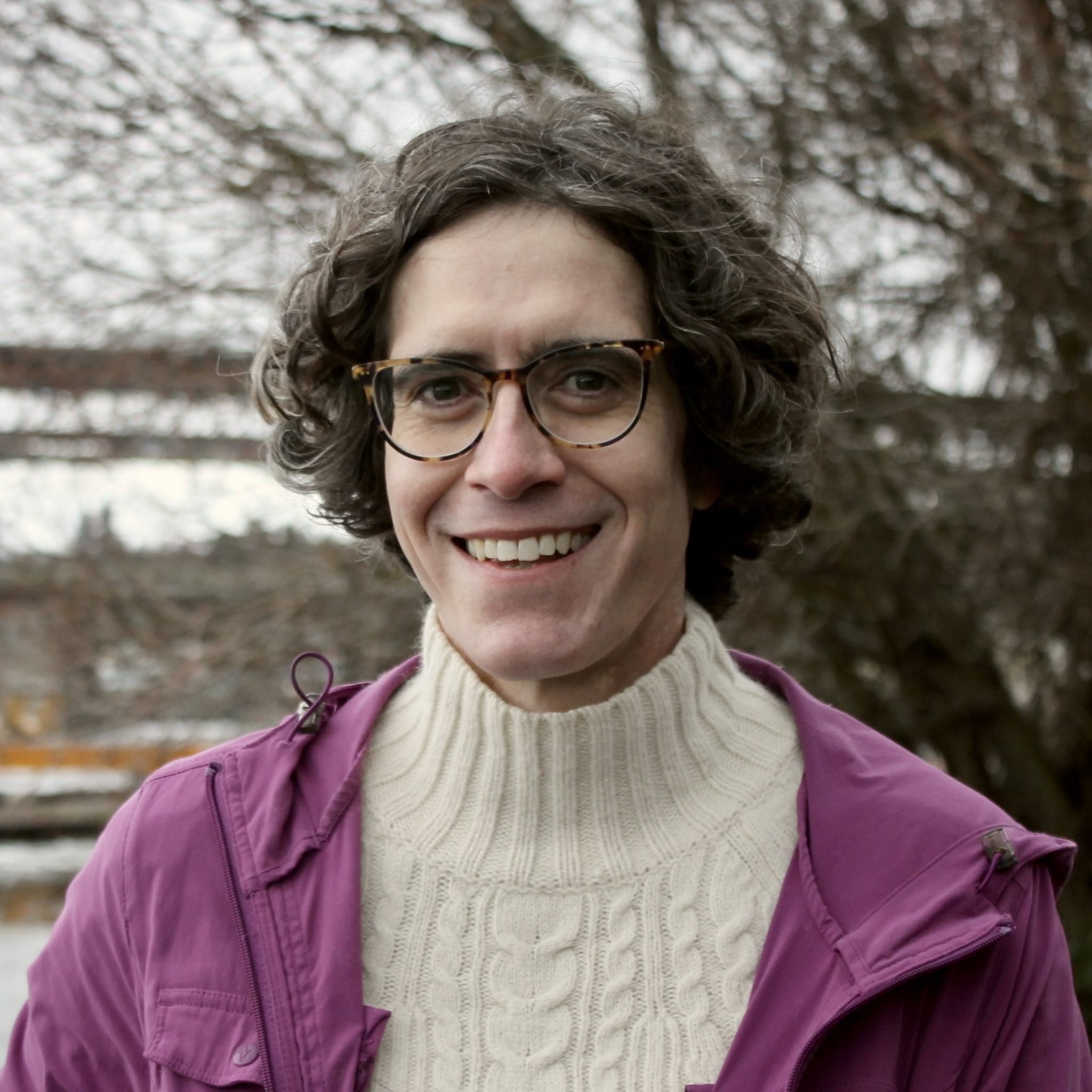 Headshot of Anima wearing glasses, a white seater, and a purple jacket