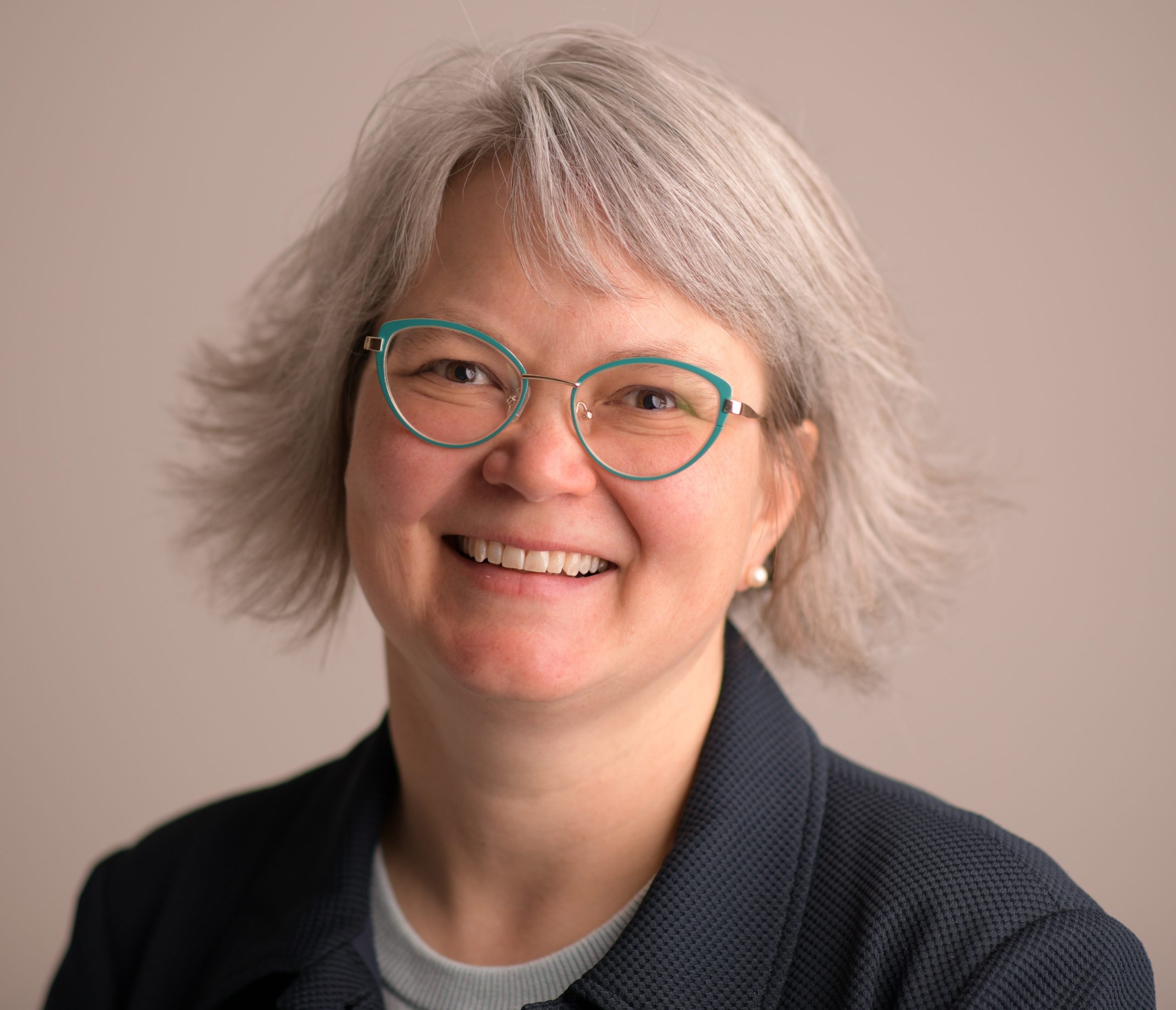 Headshot of smiling woman with silver hair and green glasses