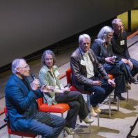 Panelists sit on chairs in front of an audience
