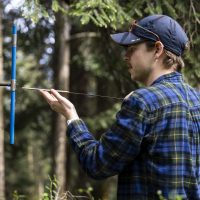 Person in a blue flannel shirt and blue hat extracts sample from a tree